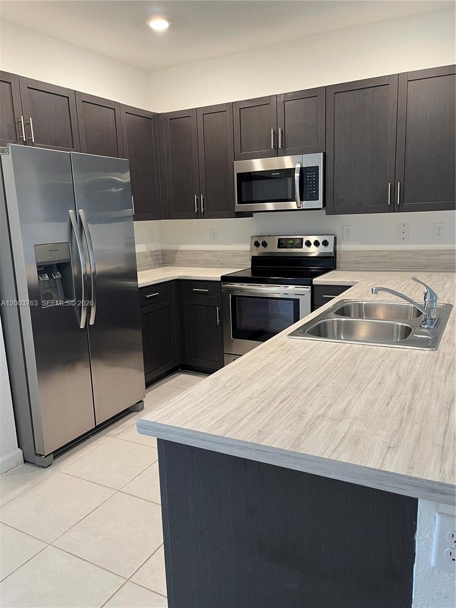 A kitchen features dark wood cabinets, stainless steel appliances, and light wood-grain laminate countertops — 10124 SW 228th Ter, Miami FL 33190, MIAMI, FL
