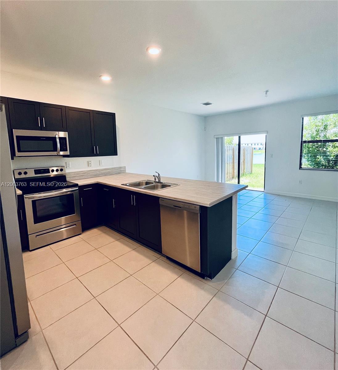 A kitchen with dark cabinets, stainless steel appliances, and tile flooring opens to a living area — 10124 SW 228th Ter, Miami FL 33190, MIAMI, FL