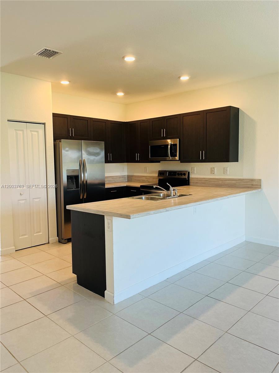 A kitchen features dark wood cabinets, stainless steel appliances, and a light-colored laminate countertop — 10124 SW 228th Ter, Miami FL 33190, MIAMI, FL