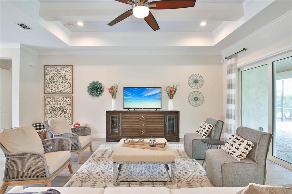 A living room features a tray ceiling, a media console, and four armchairs around an ottoman — 7808 34TH COURT E, SARASOTA, FL