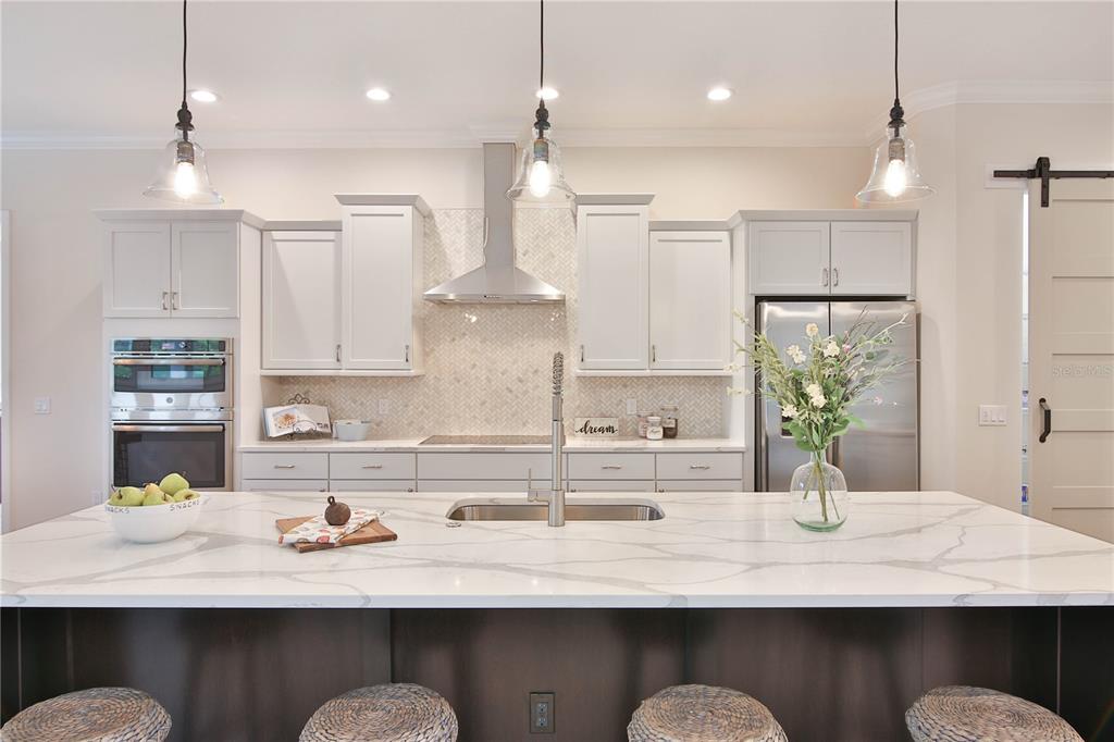 A modern kitchen features white cabinetry, a marble-patterned island, and stainless steel appliances — 7808 34TH COURT E, SARASOTA, FL