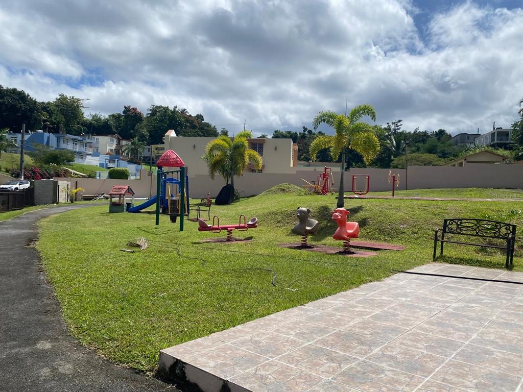 A grassy playground area features a swing set, spring riders, and a bench — Estancias del Verde CALLE 3 UNIT #71, RIO GRANDE, PR