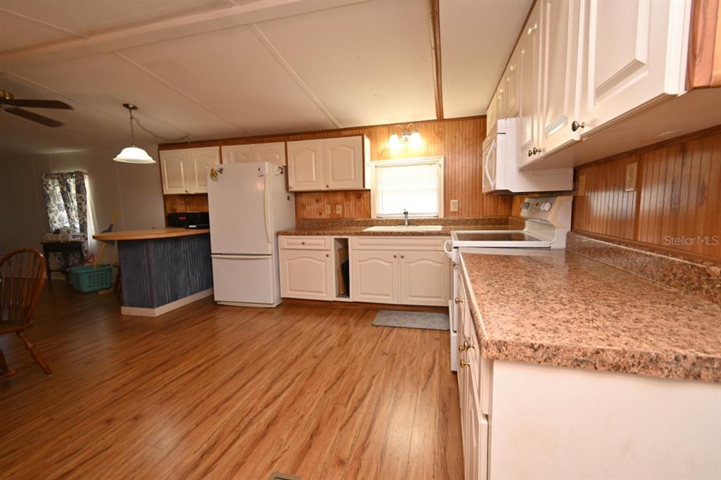 A kitchen features white cabinets, wood-paneled walls, laminate countertops, and light wood-look flooring — 34940 FRASER STREET, DADE CITY, FL