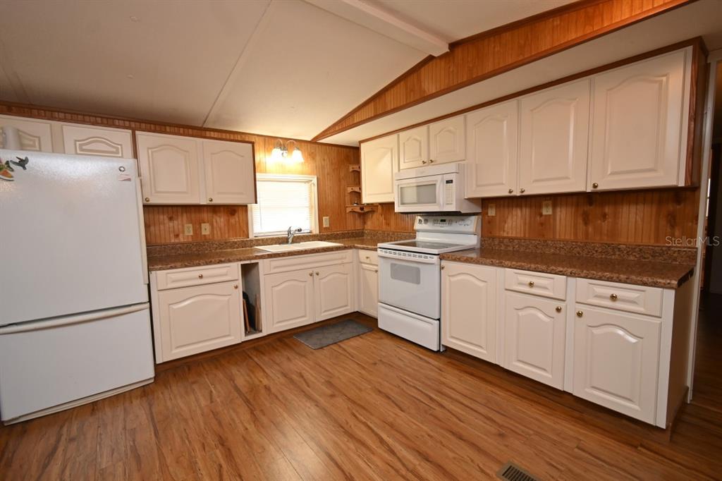 A kitchen features white cabinets, wood-paneled walls, laminate countertops, and light wood-look flooring — 34940 FRASER STREET, DADE CITY, FL