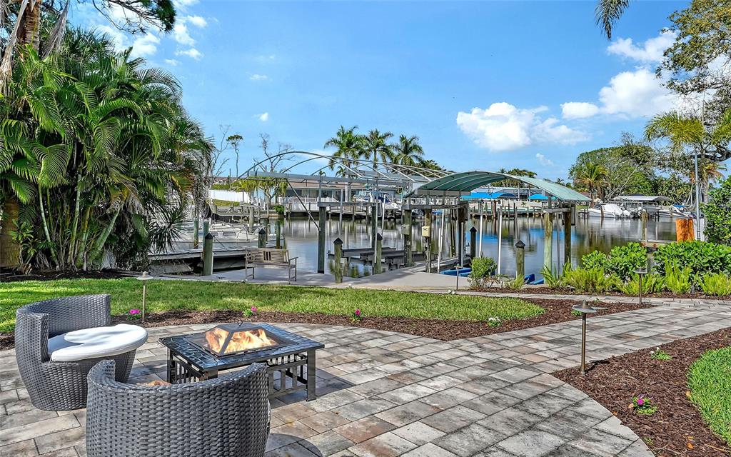A patio with a fire pit and wicker chairs overlooks a canal with boat docks — 121 HOLLY AVENUE, SARASOTA, FL