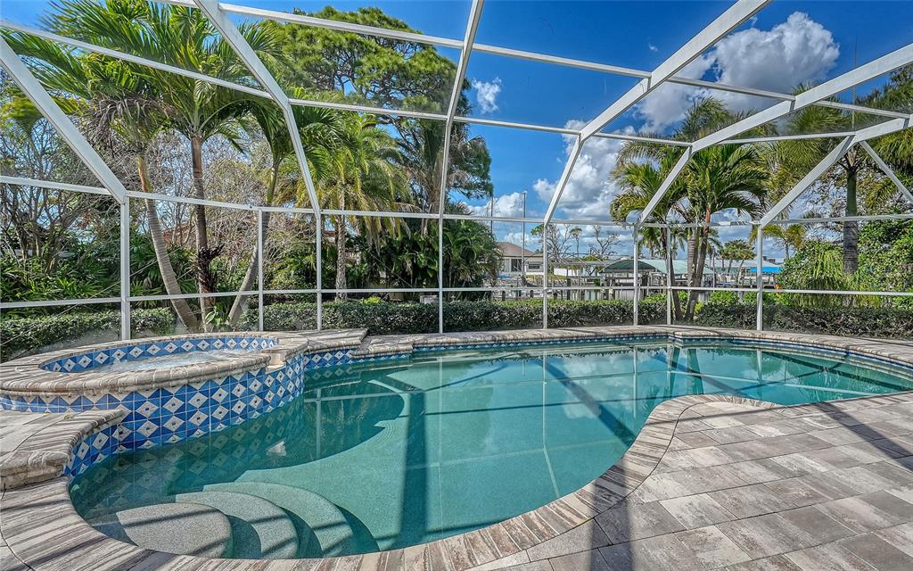 A screened-in swimming pool and hot tub with blue tile accents on a stone patio — 121 HOLLY AVENUE, SARASOTA, FL