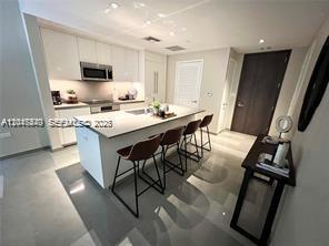 A modern kitchen features a central island with bar stools and white cabinetry — 68 SE 6th St # 906, Miami FL 33131, MIAMI, FL