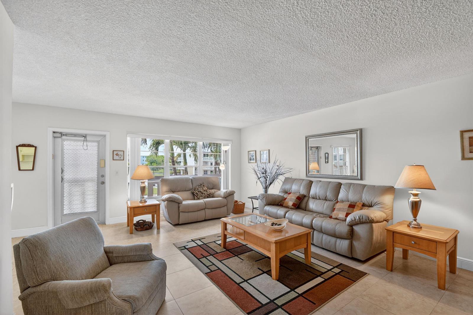 A living room features light-colored tile floors, a textured ceiling, and a geometric area rug — 202 Wellington D, West Palm Beach FL 33417, WEST PALM BEACH, FL