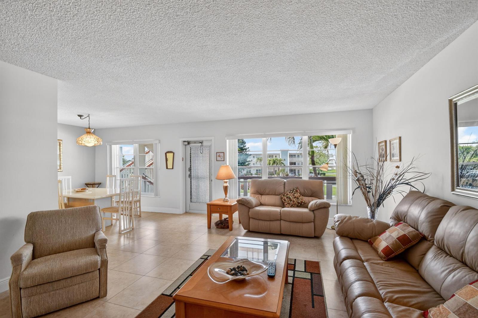 A living room with tile floors, a popcorn ceiling, and a dining area in the background — 202 Wellington D, West Palm Beach FL 33417, WEST PALM BEACH, FL