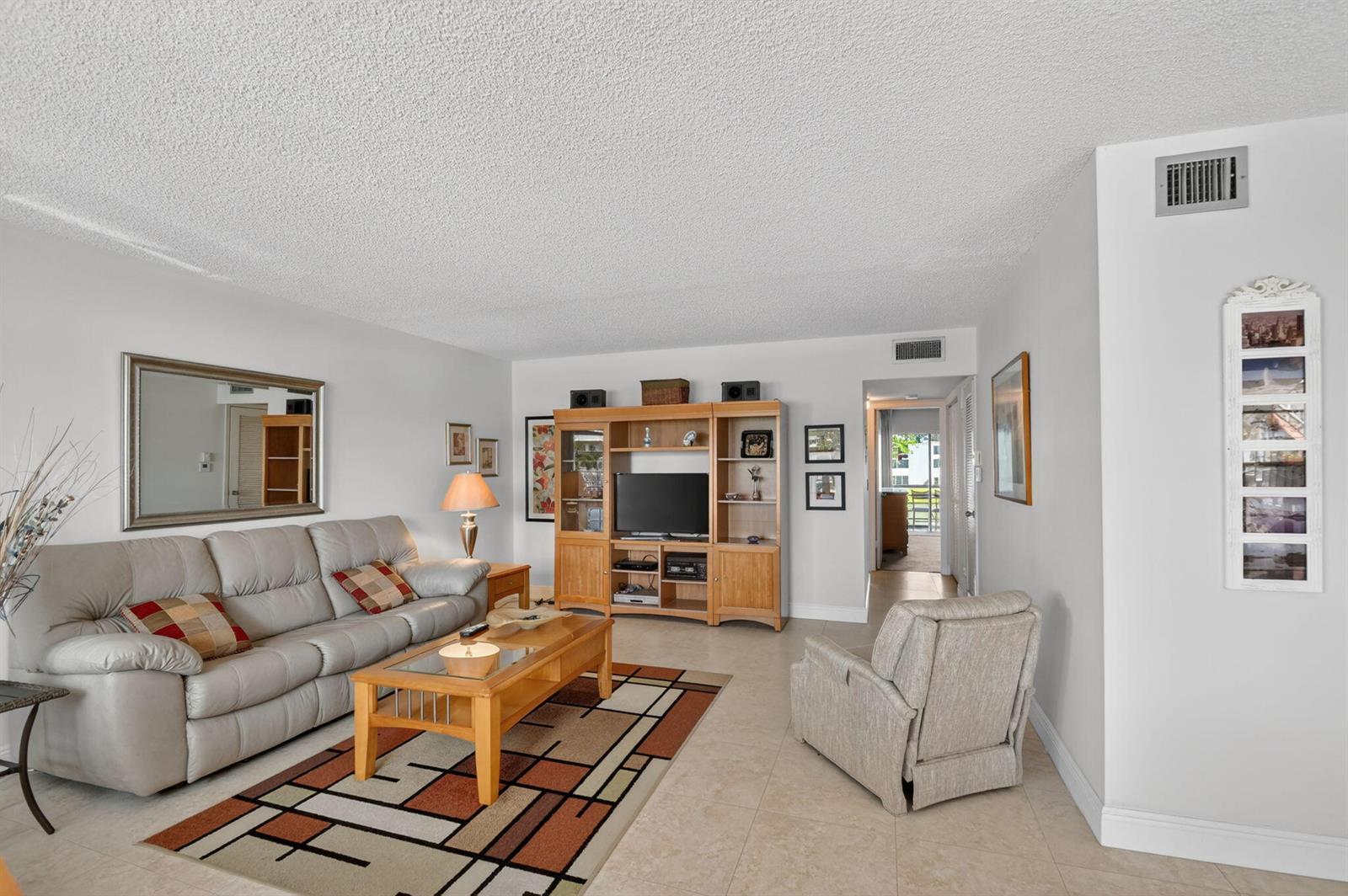 A living room features a light gray sofa, a wooden entertainment center, and a patterned rug — 202 Wellington D, West Palm Beach FL 33417, WEST PALM BEACH, FL