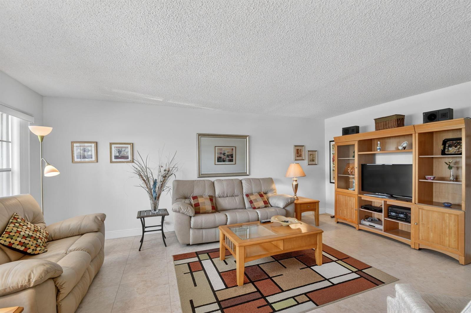 A living room features light-colored tile floors, a beige sofa, and a wooden entertainment center — 202 Wellington D, West Palm Beach FL 33417, WEST PALM BEACH, FL