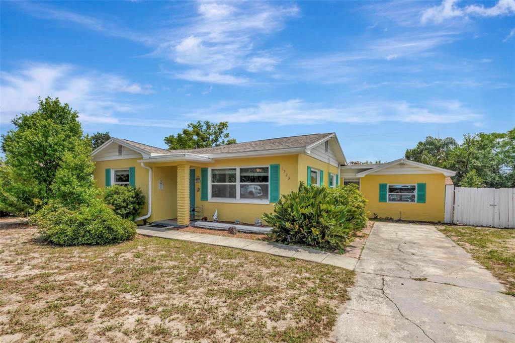 A yellow single-story house with teal shutters and a concrete driveway under a blue sky — 1223 UNION STREET, CLEARWATER, FL