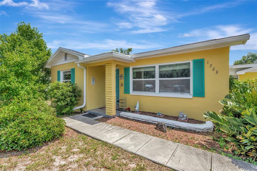 A yellow single-story house with teal shutters and a concrete walkway leading to the entrance — 1223 UNION STREET, CLEARWATER, FL