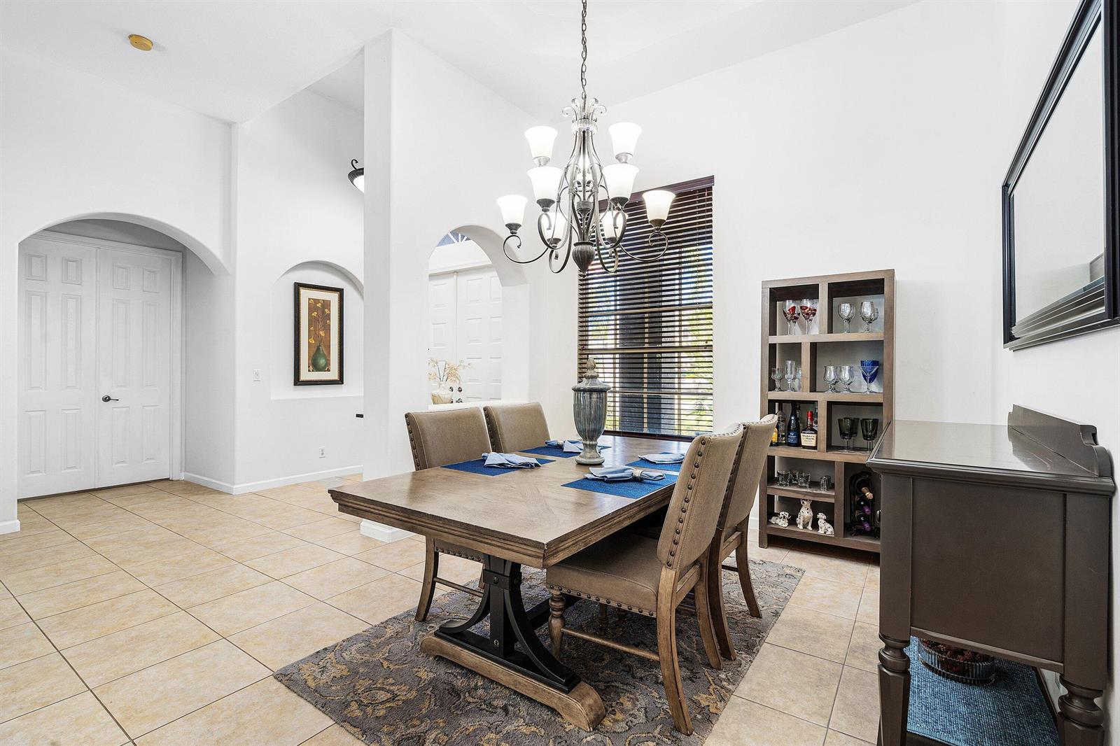 A dining room features a wooden table, upholstered chairs, a chandelier, and a shelving unit — 4972 Forest Dale Drive, Lake Worth FL 33449, LAKE WORTH, FL