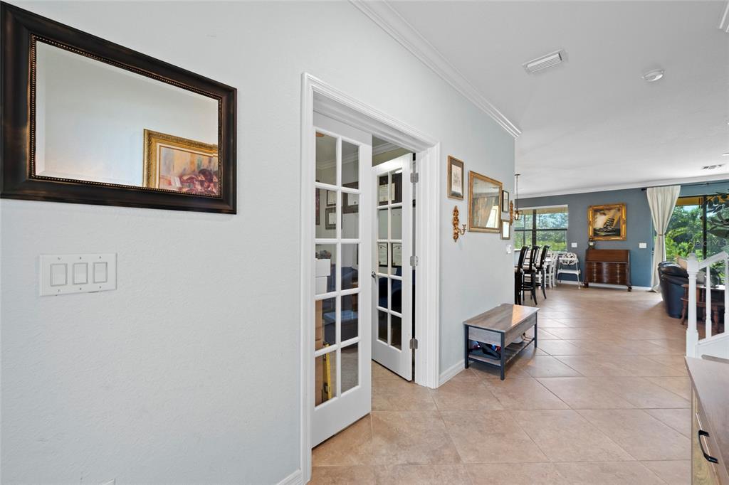 A hallway with tile flooring leads to a dining area and a room with French doors — 12600 RICHEZZA DRIVE, VENICE, FL