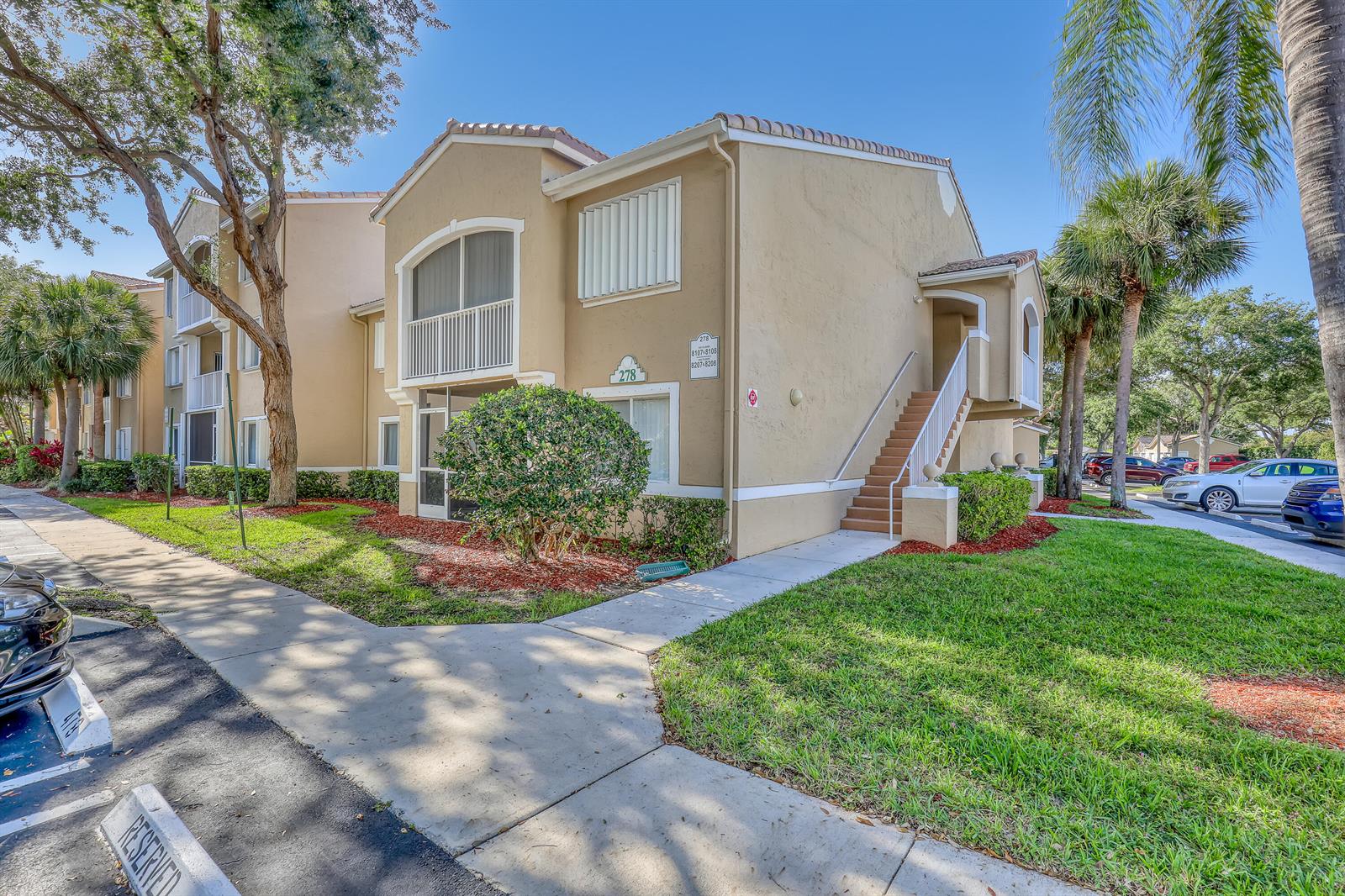 A two-story tan apartment building features a staircase, balconies, and surrounding landscaping — 278 Village Boulevard # 8208, Tequesta FL 33469, TEQUESTA, FL