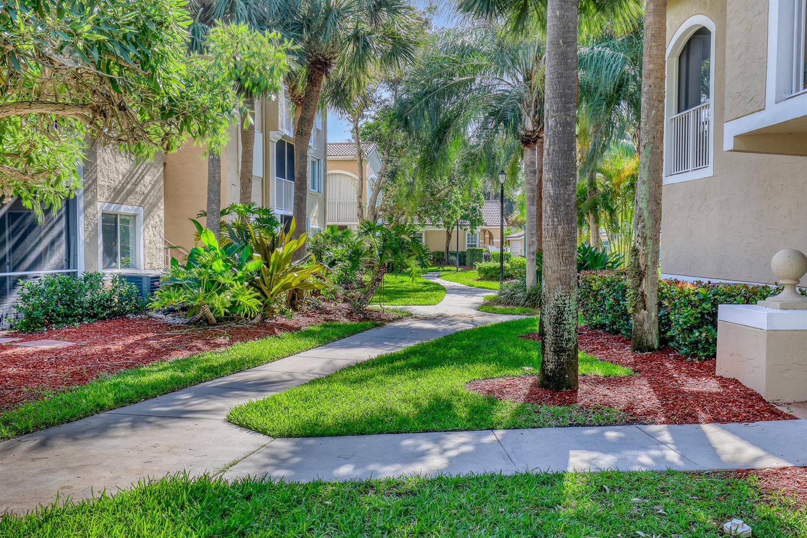 A concrete walkway winds through a landscaped courtyard between two multi-story apartment buildings — 278 Village Boulevard # 8208, Tequesta FL 33469, TEQUESTA, FL