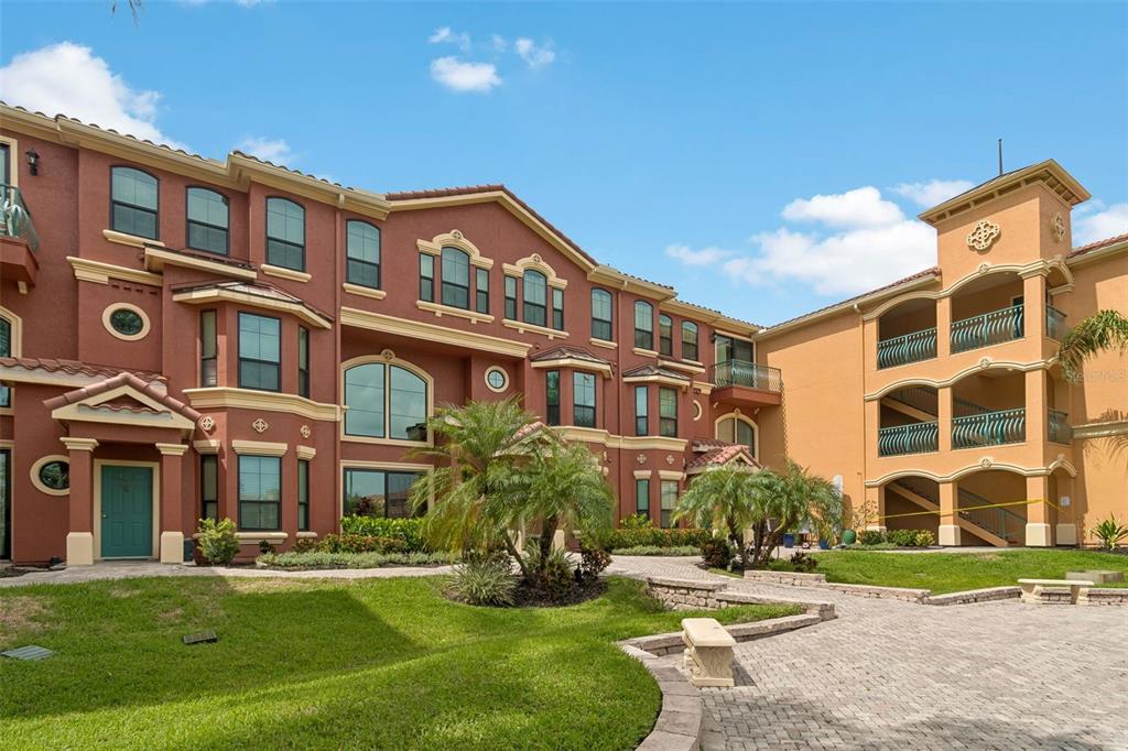 An exterior view of a multi-story apartment building with red and tan stucco facades — 2717 VIA CIPRIANI UNIT 623A, CLEARWATER, FL