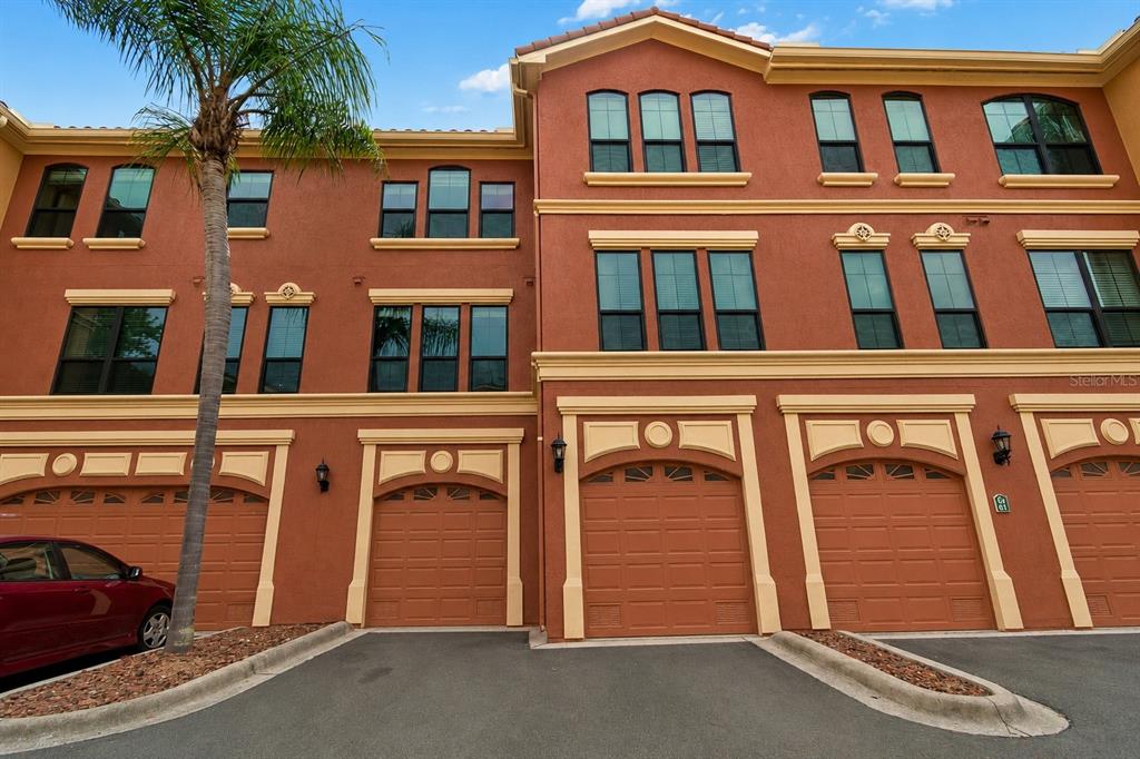 A multi-story townhouse exterior with a red stucco facade, multiple garage doors, and palm trees — 2717 VIA CIPRIANI UNIT 623A, CLEARWATER, FL