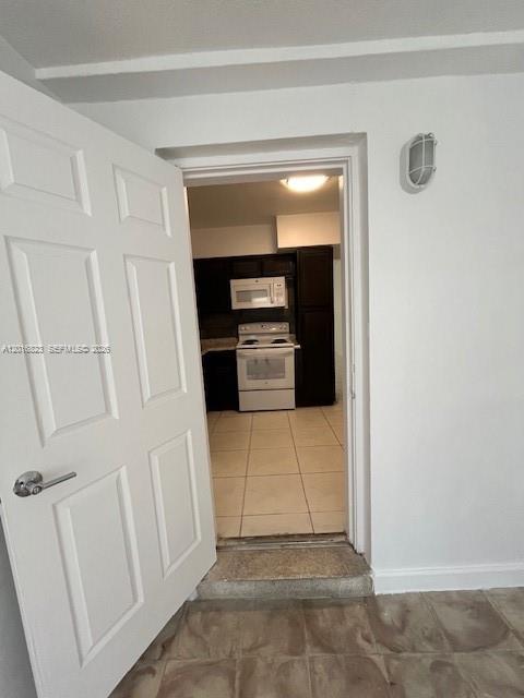 A white door opens into a kitchen featuring dark cabinets, a white stove, and tile flooring — 901 SW 4th Ter, Hallandale Beach FL 33009, HALLANDALE BEACH, FL