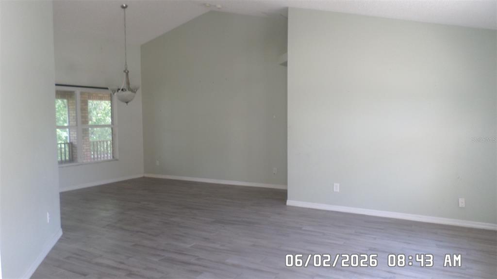 An empty living room features vaulted ceilings, light green walls, and gray wood-look flooring — 1638 W AKRON DRIVE, DELTONA, FL