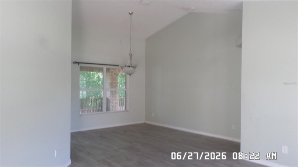 An empty room with vaulted ceilings, gray wood-look flooring, and a hanging light fixture — 1638 W AKRON DRIVE, DELTONA, FL