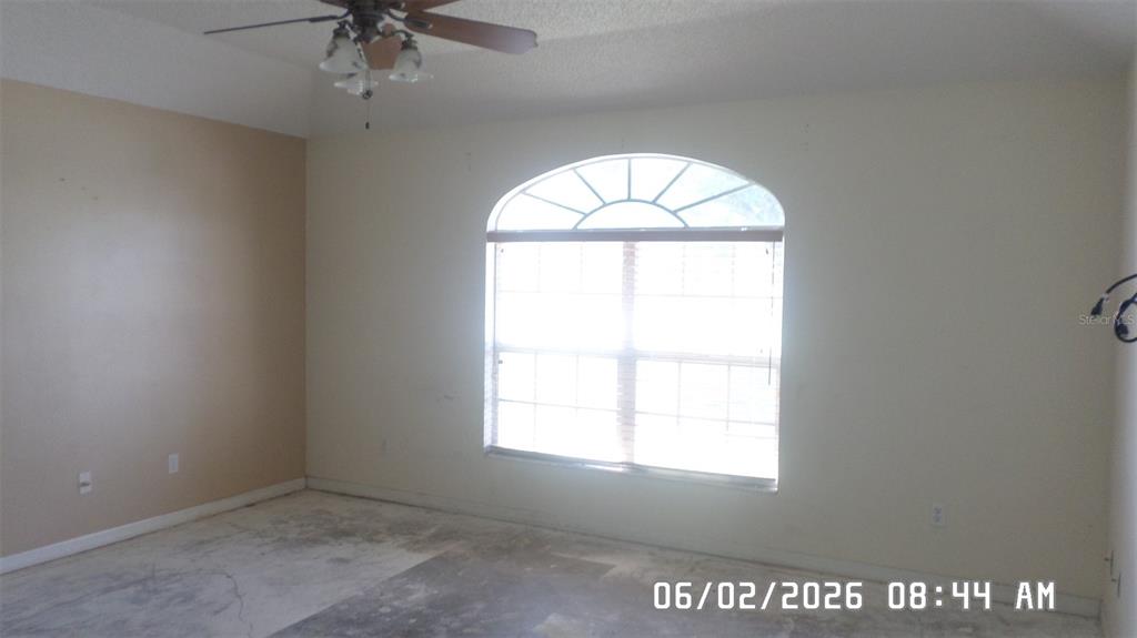 An empty room features a ceiling fan, a large arched window, and unfinished concrete flooring — 1638 W AKRON DRIVE, DELTONA, FL