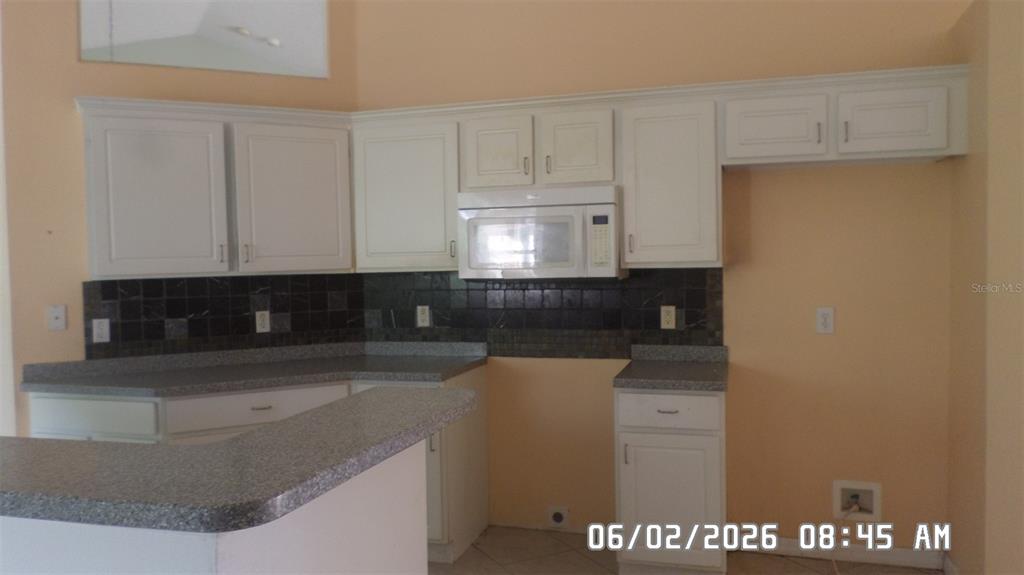 A kitchen features white cabinets, dark tiled backsplash, and gray laminate countertops — 1638 W AKRON DRIVE, DELTONA, FL