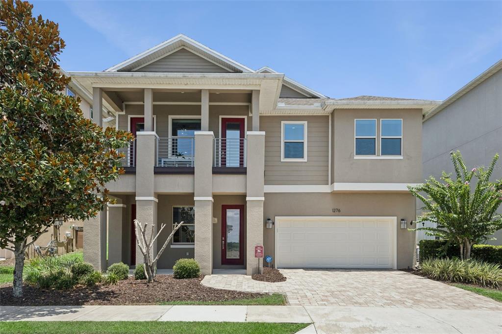 A two-story house with a beige stucco exterior, a red front door, and a balcony — 1276 DORA PARC LANE, MOUNT DORA, FL