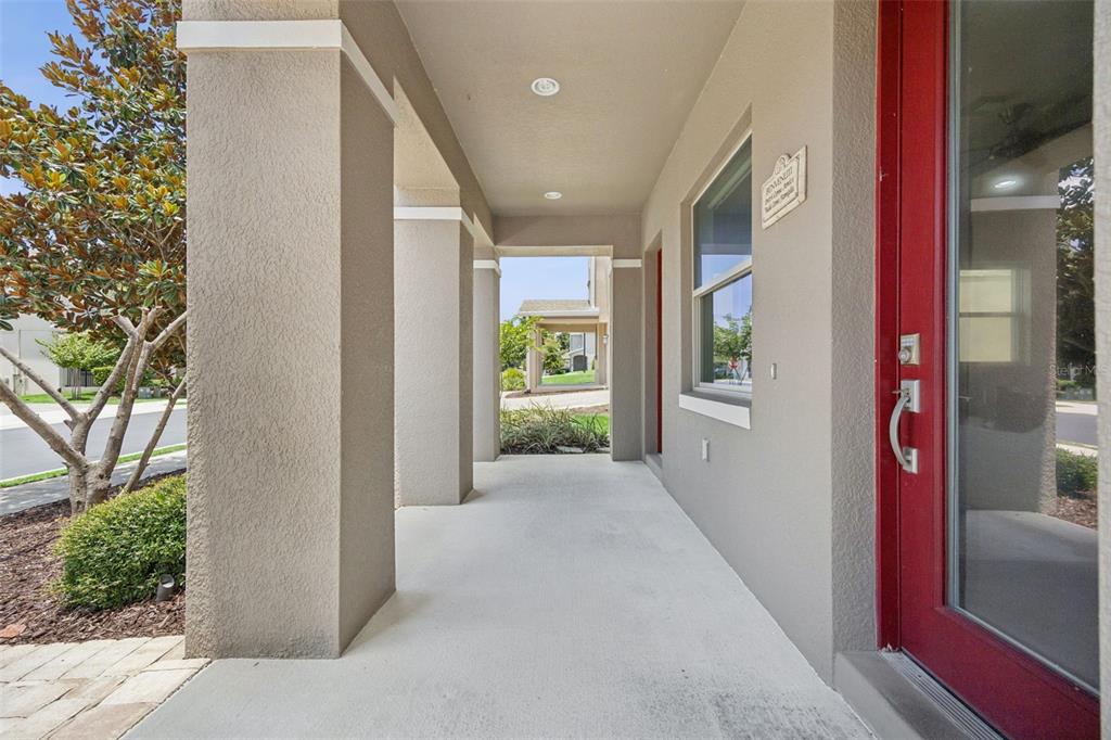 A covered concrete porch features square columns and a bright red front door — 1276 DORA PARC LANE, MOUNT DORA, FL