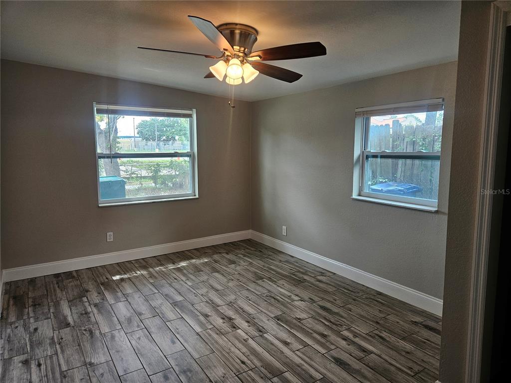 An empty bedroom features light gray walls, wood-look tile flooring, and a ceiling fan — 15165 HARDING AVENUE, CLEARWATER, FL