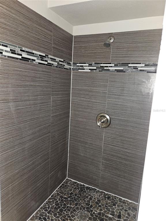 A walk-in shower features gray horizontal-patterned wall tiles, a decorative mosaic accent strip, and pebbles — 15165 HARDING AVENUE, CLEARWATER, FL