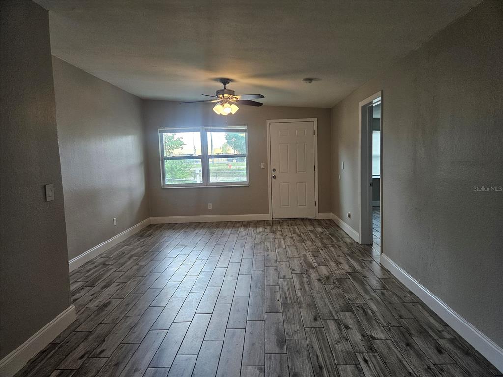 A living room features gray wood-look tile flooring, a ceiling fan, and a white entry door — 15165 HARDING AVENUE, CLEARWATER, FL