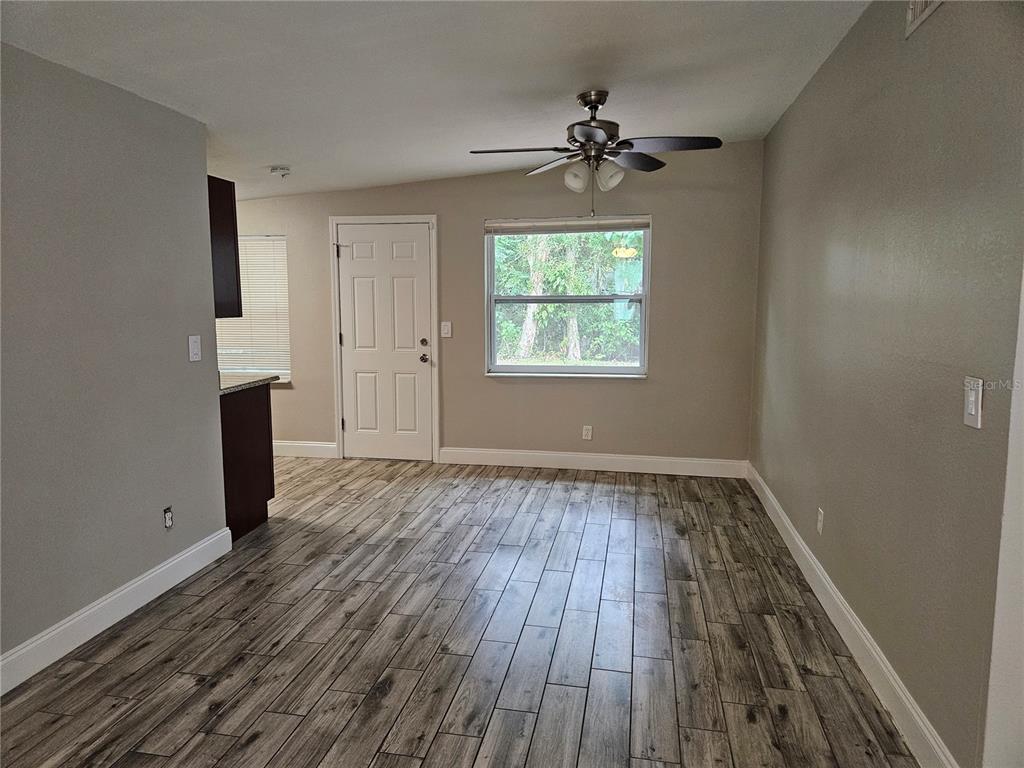 An empty room features wood-look tile flooring, a ceiling fan, and a white exterior door — 15165 HARDING AVENUE, CLEARWATER, FL