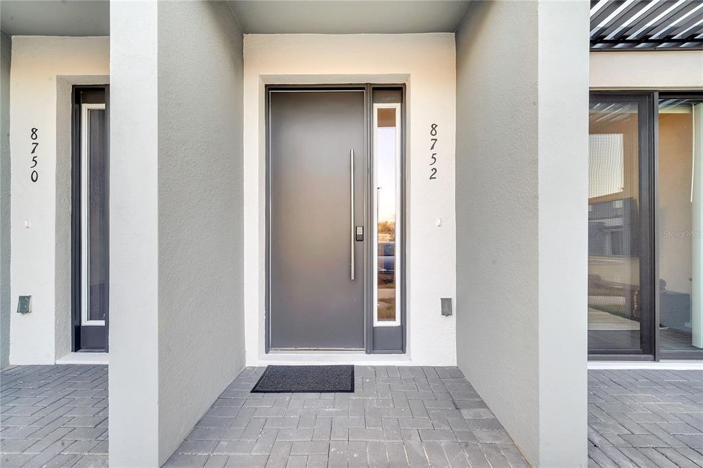 A modern gray front door with a vertical handle is centered between two building entrances — 8752 GOOD VIBES PLACE, KISSIMMEE, FL