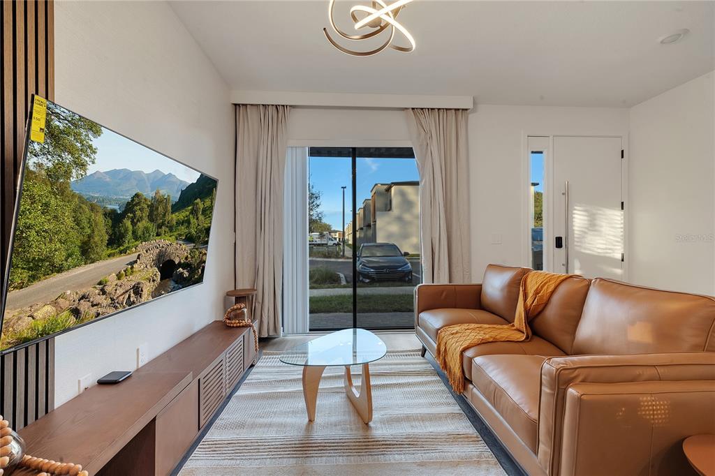 A living room features a brown leather sofa, a glass coffee table, and a wall-mounted television — 8752 GOOD VIBES PLACE, KISSIMMEE, FL