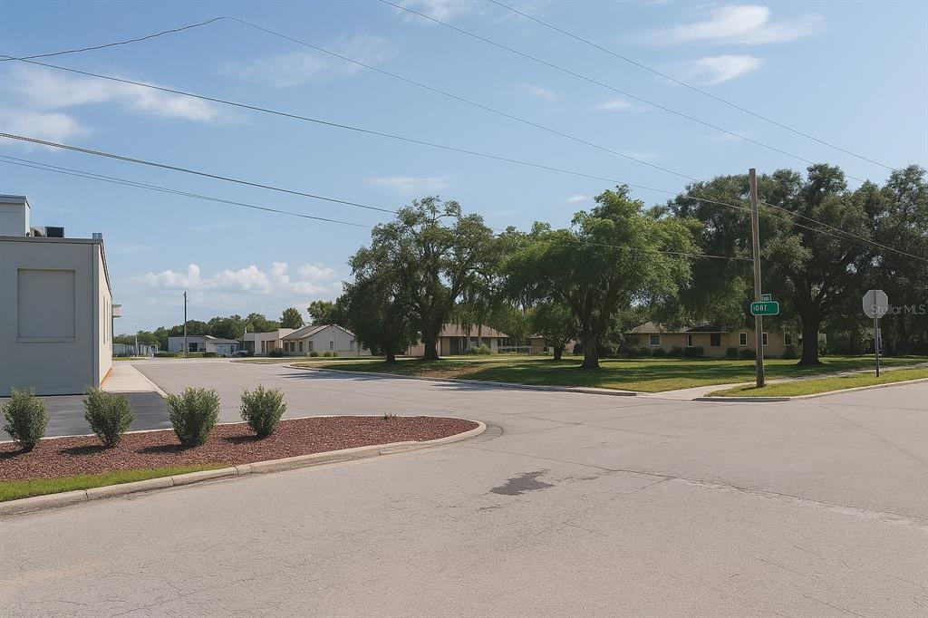 A paved street intersection features a commercial building, residential houses, and mature trees — 203 EMERALD AVENUE, LAKE WALES, FL