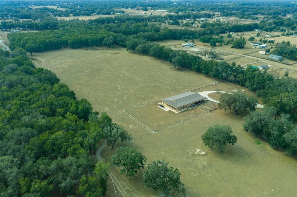 An aerial view shows a large metal-roofed building situated in a fenced, grassy pasture — 2051 SE 155TH STREET, SUMMERFIELD, FL