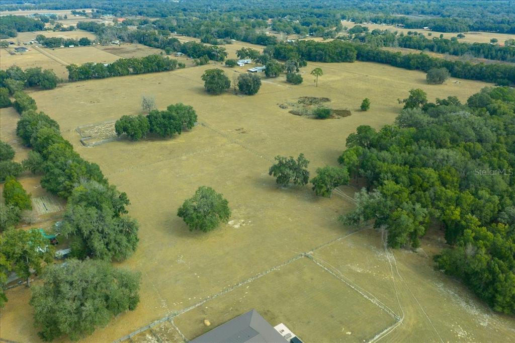 An aerial view shows a large, fenced grassy pasture with scattered trees and a house roof — 2051 SE 155TH STREET, SUMMERFIELD, FL