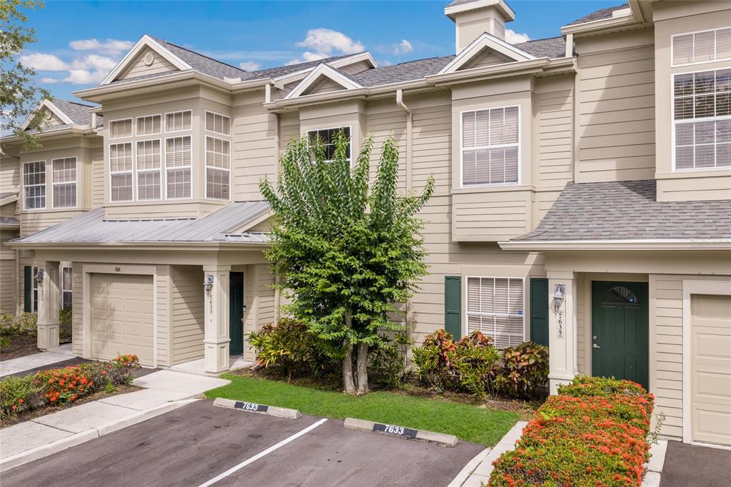 The exterior view shows a two-story townhouse with beige siding, a green door, and parking — 7633 PLANTATION CIRCLE UNIT 7633, UNIVERSITY PARK, FL