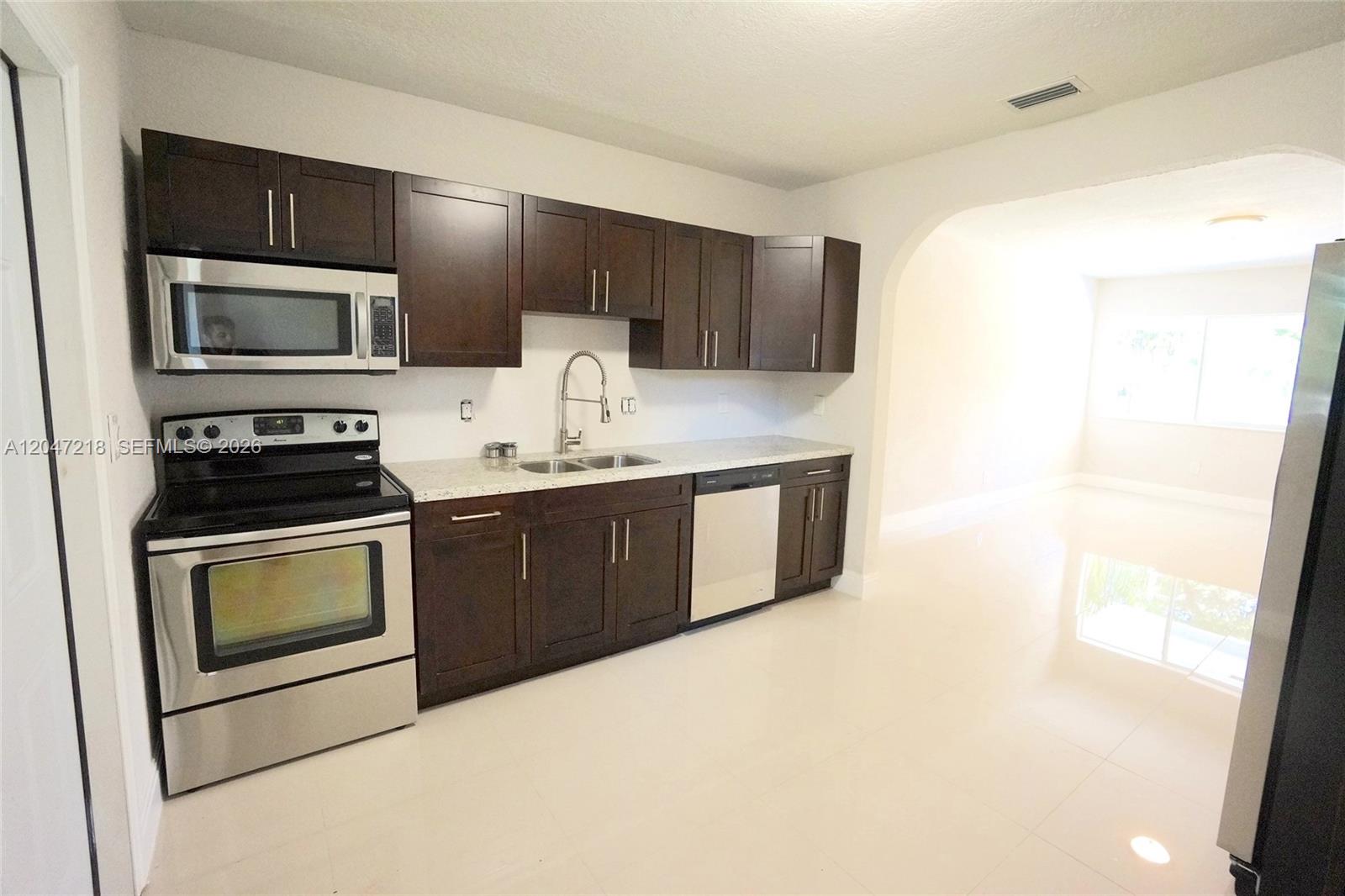 A kitchen features dark wood cabinets, stainless steel appliances, and light-colored countertops and flooring — 1497 NE 118th Ter # 2, Miami FL 33161, MIAMI, FL