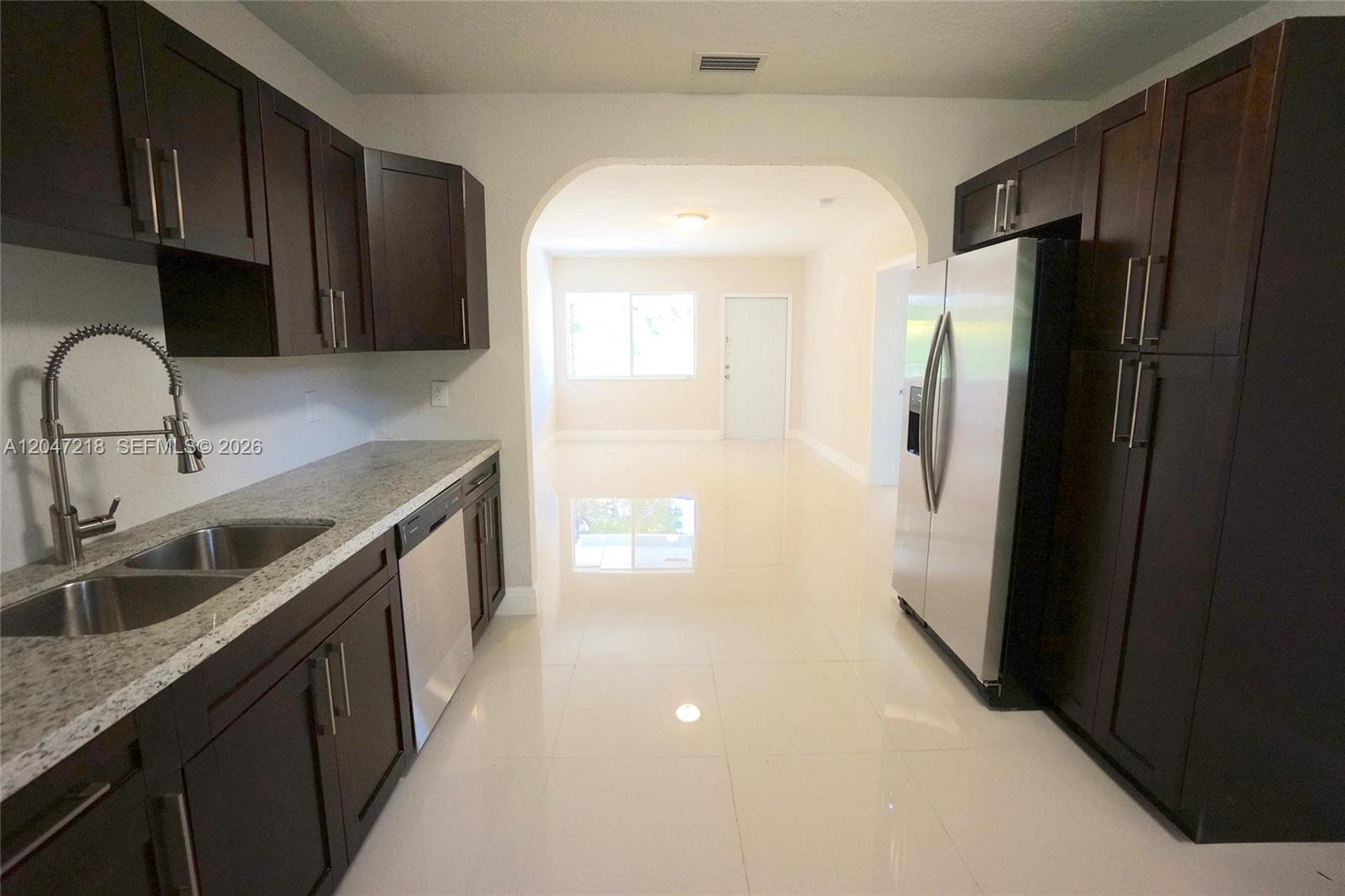 A kitchen features dark wood cabinets, granite countertops, stainless steel appliances, and white tile flooring — 1497 NE 118th Ter # 2, Miami FL 33161, MIAMI, FL