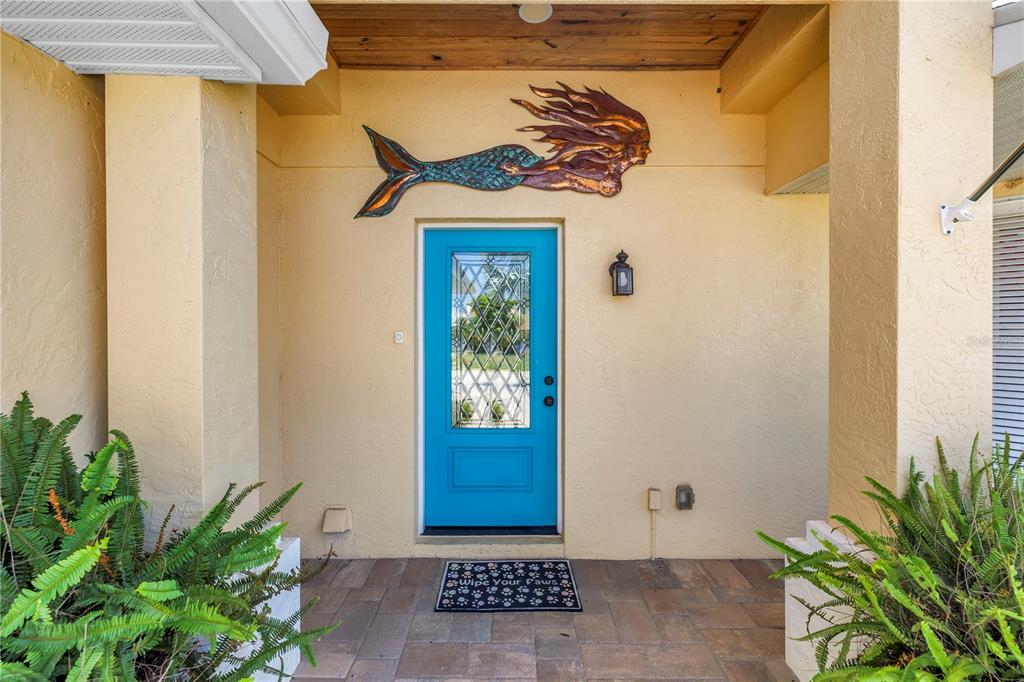 A bright blue front door sits under a covered porch with a mermaid wall sculpture — 6113 45TH STREET W, BRADENTON, FL
