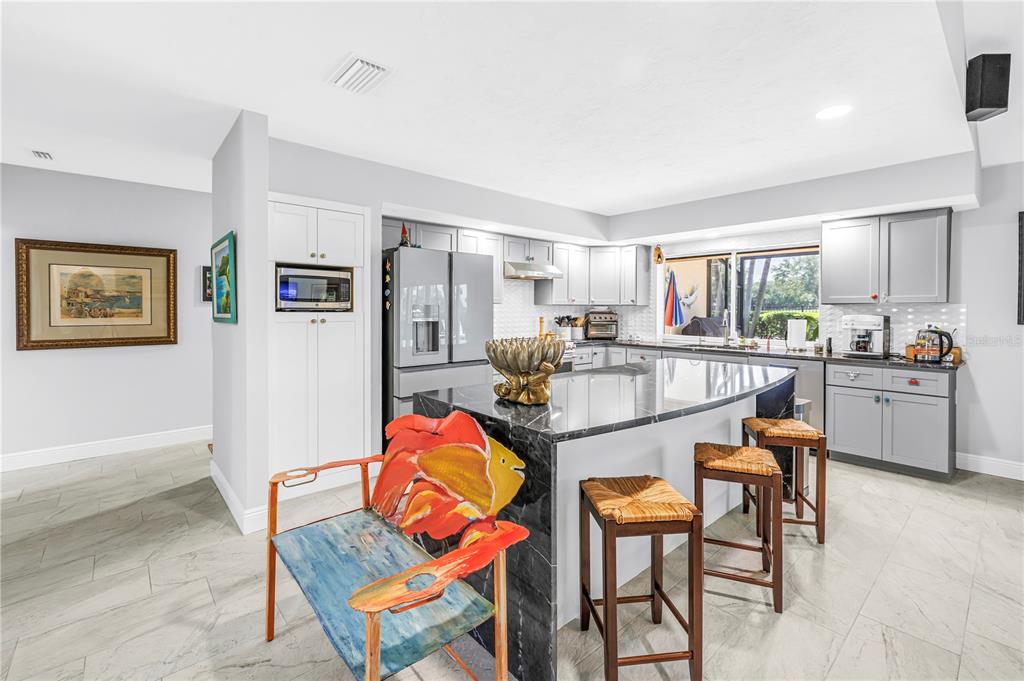 A kitchen features a black marble island, gray cabinetry, and a colorful fish-shaped chair — 6113 45TH STREET W, BRADENTON, FL