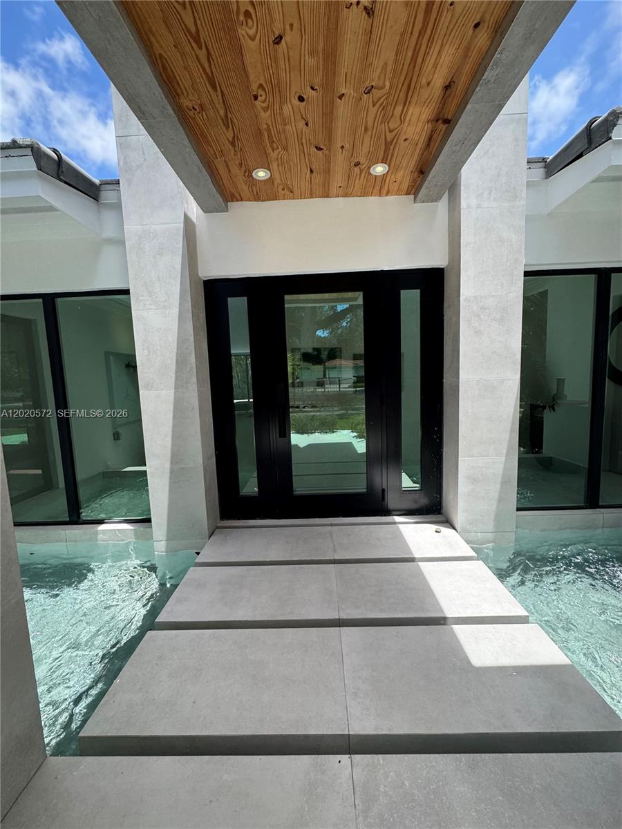 A modern entryway features a floating concrete walkway over a water feature leading to glass doors — 439 Hardee Rd, Coral Gables FL 33146, CORAL GABLES, FL
