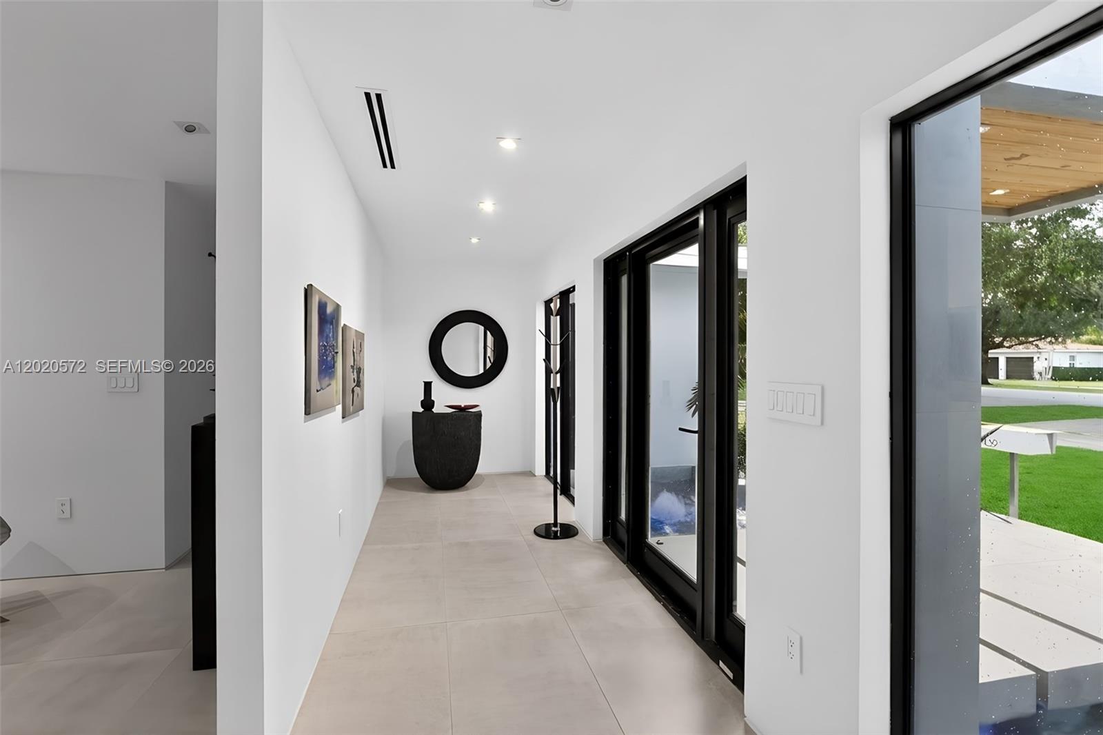 A minimalist hallway features white walls, large-format tile flooring, and black-framed glass doors — 439 Hardee Rd, Coral Gables FL 33146, CORAL GABLES, FL