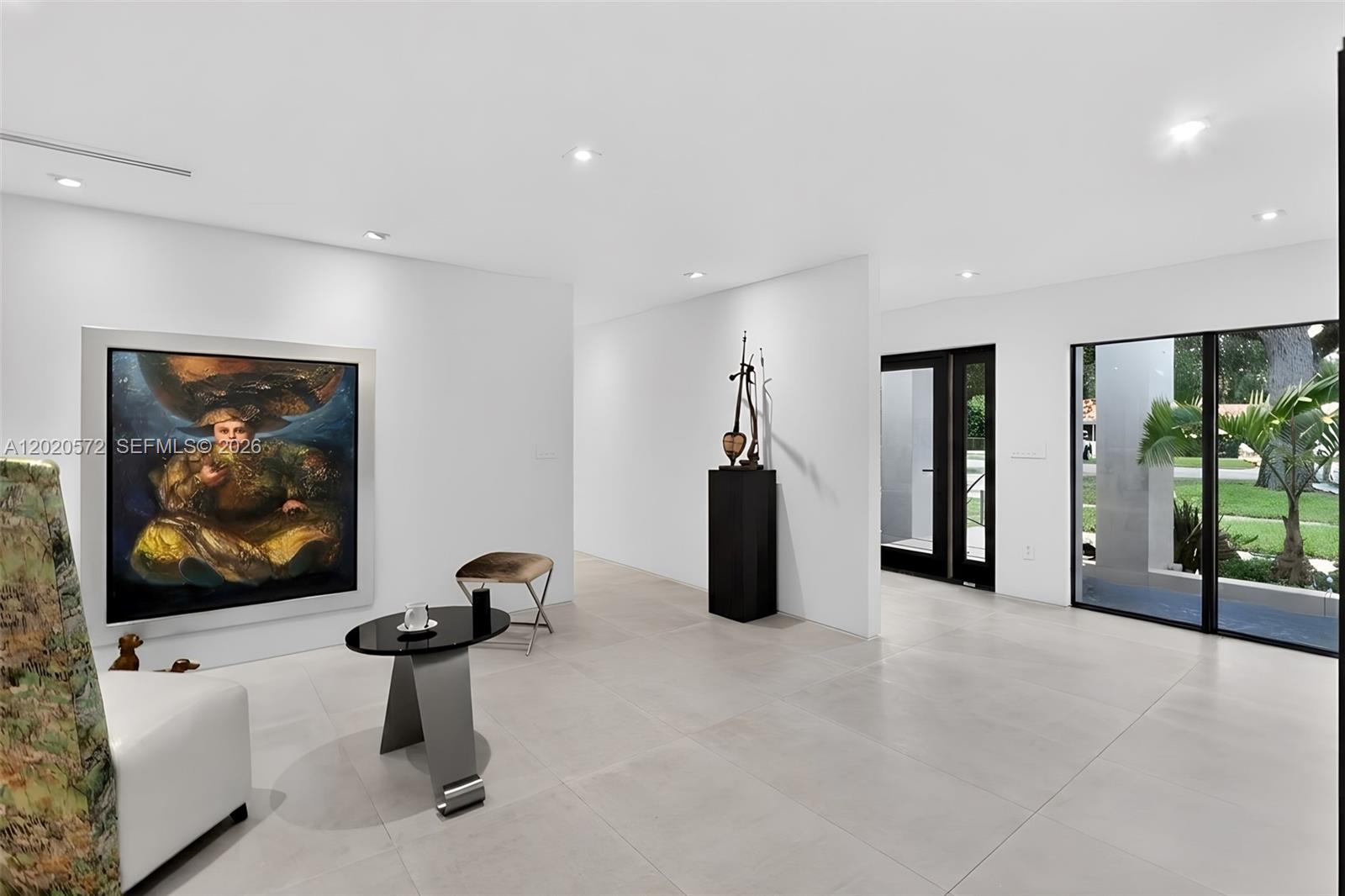 A minimalist white room features large-format tile flooring, a prominent painting, and glass sliding doors — 439 Hardee Rd, Coral Gables FL 33146, CORAL GABLES, FL
