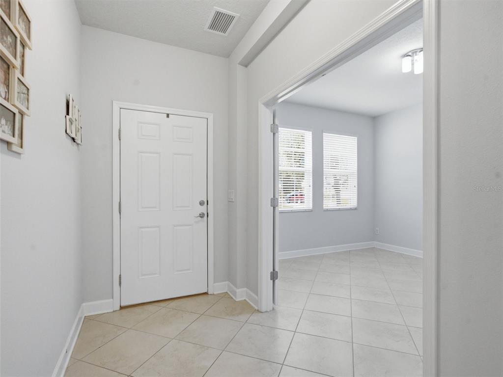 A white front door opens into a tiled entryway next to an adjacent room — 21613 SOUTHERN CHARM DRIVE UNIT DR, LAND O LAKES, FL