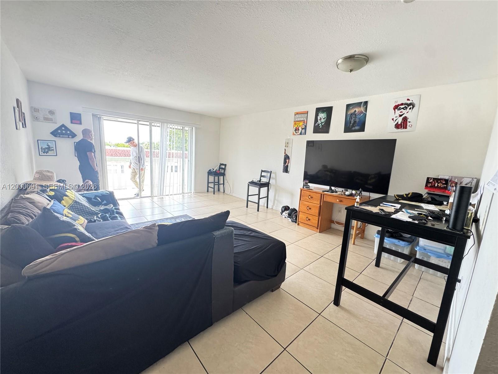 A living room features tile flooring, a large television, a sofa, and a sliding glass door — 15201 NE 6th Ave # C304, Miami FL 33162, MIAMI, FL