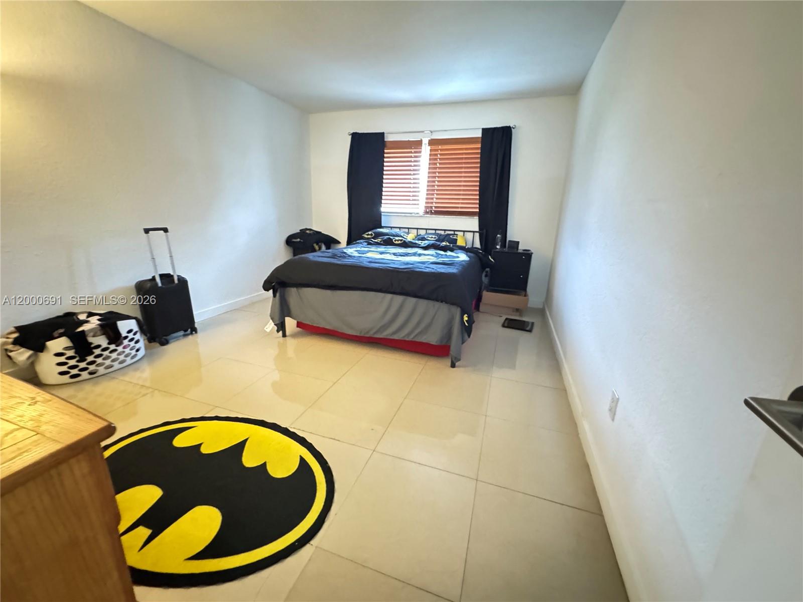 A bedroom features light tile flooring, a Batman-themed rug, and a bed with dark bedding — 15201 NE 6th Ave # C304, Miami FL 33162, MIAMI, FL